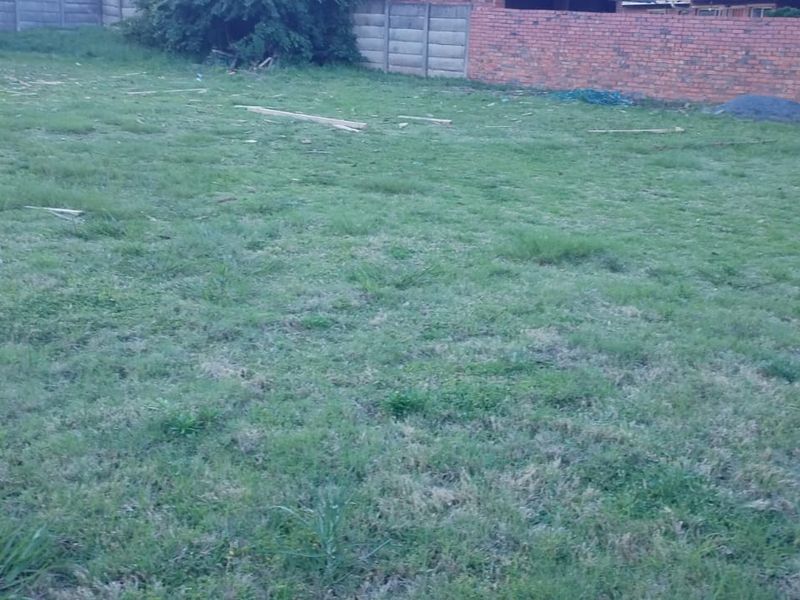 A vacant residential plot featuring grass coverage and established brick and precast concrete boundary walls.