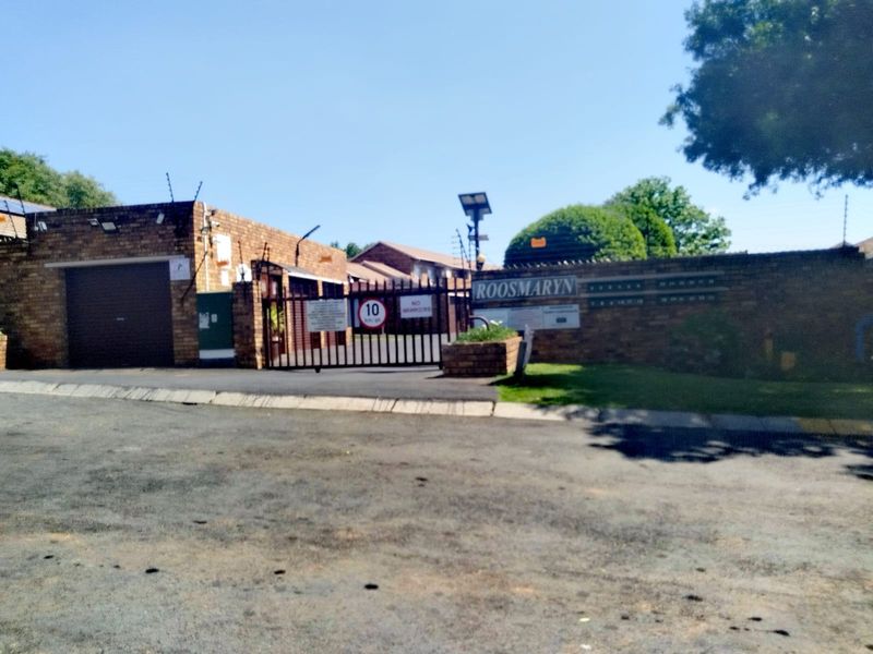 Front entrance view of the Roosmaryn townhouse complex featuring a secure gated access point, brick boundary walls, and electric fencing.