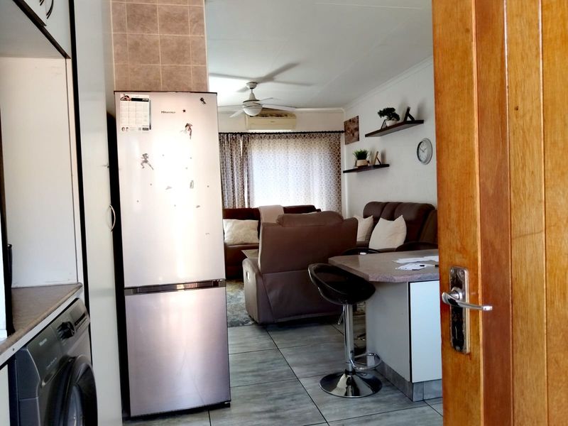 Open-plan living area featuring tiled flooring, a ceiling fan, air conditioning, and a breakfast bar connecting to the kitchen space.
