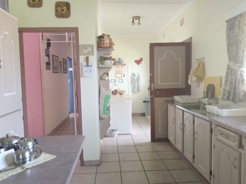 A functional kitchen featuring tiled flooring, built-in cabinetry with laminate countertops, and a classic stable door leading to the adjacent living area.