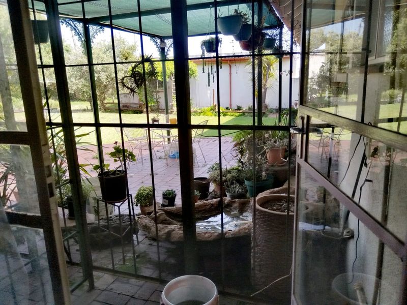 A covered patio area featuring a metal security gate, paved flooring, and a shade cloth canopy, overlooking a garden space.