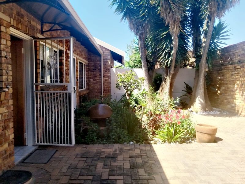 A private rear courtyard featuring brick paving, established garden beds, a water feature, and secure access to the townhouse interior.