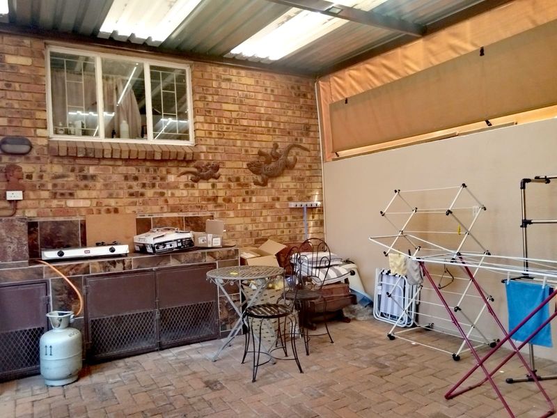 Covered outdoor patio area featuring a brick wall, built-in tiled counter with gas hob, and paved flooring, suitable for outdoor entertaining.