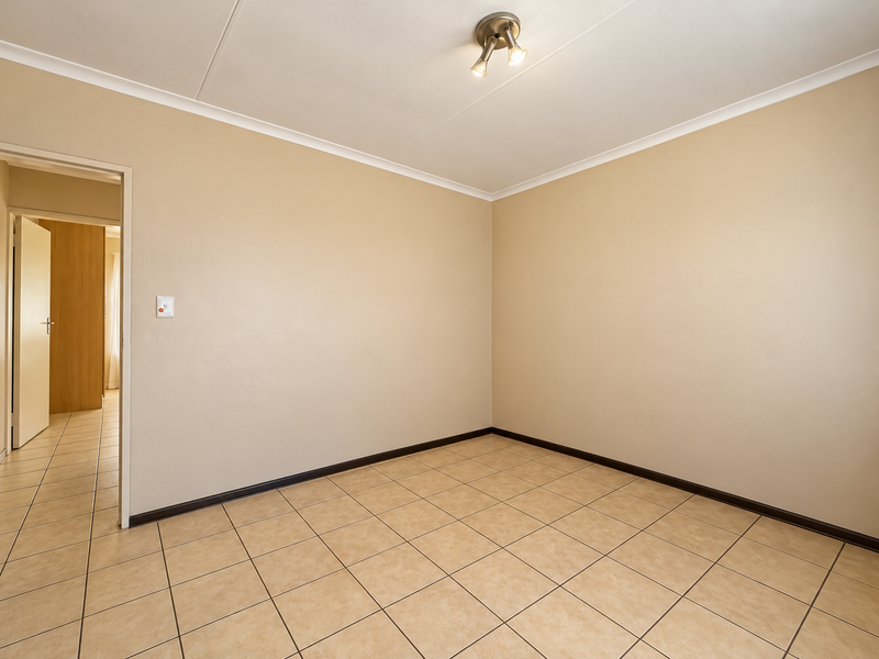 A clean, empty bedroom featuring neutral wall paint, ceramic floor tiles, and a modern ceiling spotlight fixture, offering a versatile space for customization.