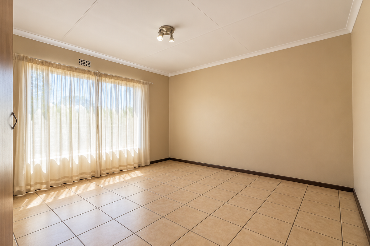 A bright, empty bedroom featuring neutral tiled flooring, coved ceilings, and a built-in cupboard, offering a clean canvas for personalization.