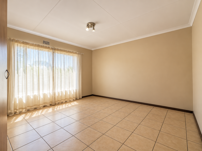 A bright, empty bedroom featuring neutral tiled flooring, coved ceilings, and a built-in cupboard, offering a clean canvas for personalization.