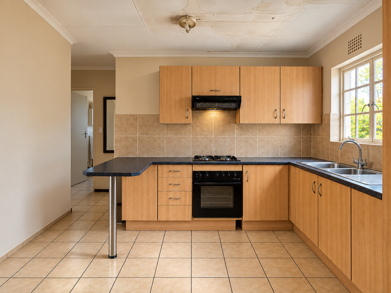 A functional kitchen featuring light wood cabinetry, built-in oven, gas hob, and breakfast bar, requiring ceiling repairs due to visible water damage.