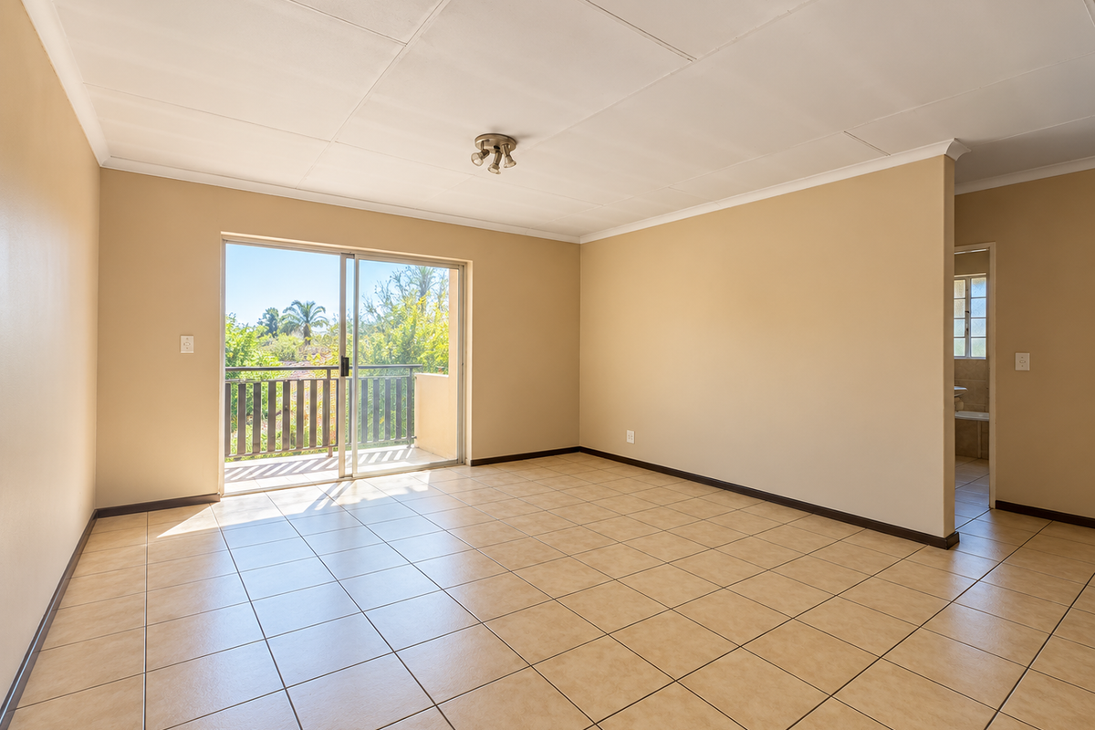 Spacious, sunlit living area featuring neutral tiled flooring, a coved ceiling, and a sliding glass door providing direct access to a private balcony.