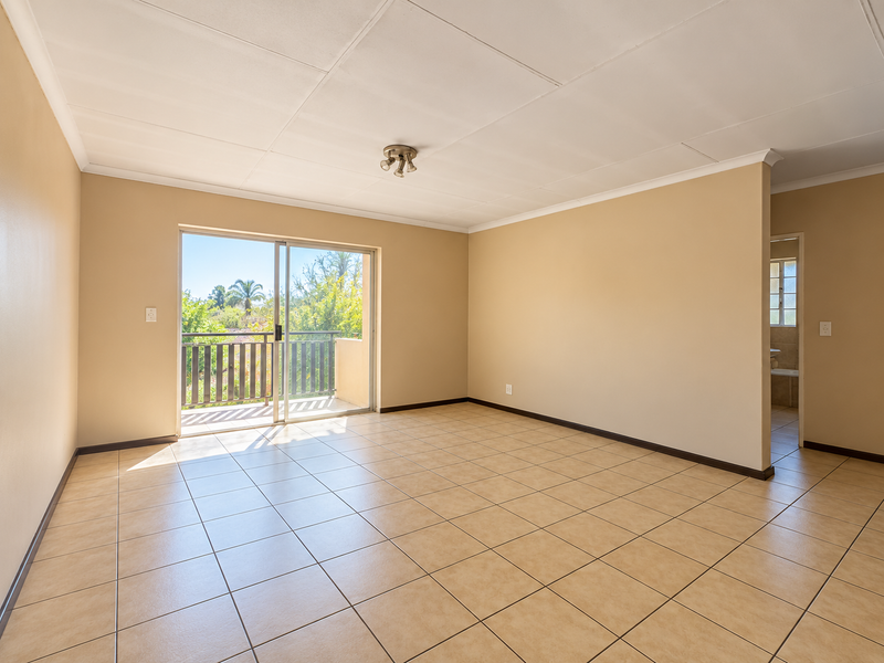 Spacious, sunlit living area featuring neutral tiled flooring, a coved ceiling, and a sliding glass door providing direct access to a private balcony.