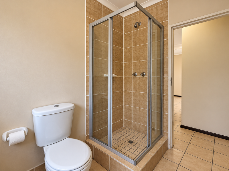 A functional bathroom featuring a corner shower enclosure with tiled walls and a standard toilet, finished with neutral floor tiles.