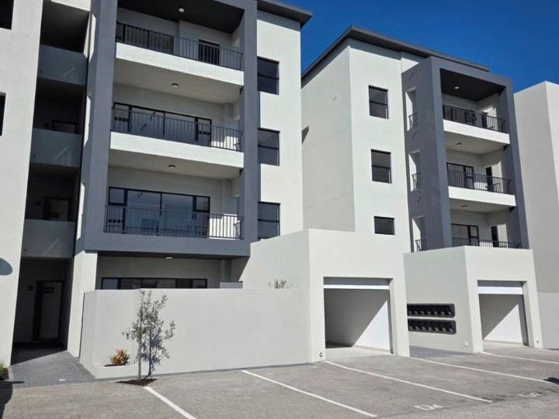 Modern multi-story apartment complex featuring contemporary facade design, private balconies, and dedicated covered parking bays with paved driveway access.