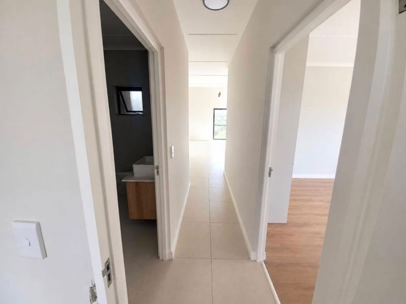 A bright, modern hallway featuring neutral tiled flooring, connecting to adjacent rooms with laminate flooring and clean, minimalist finishes.