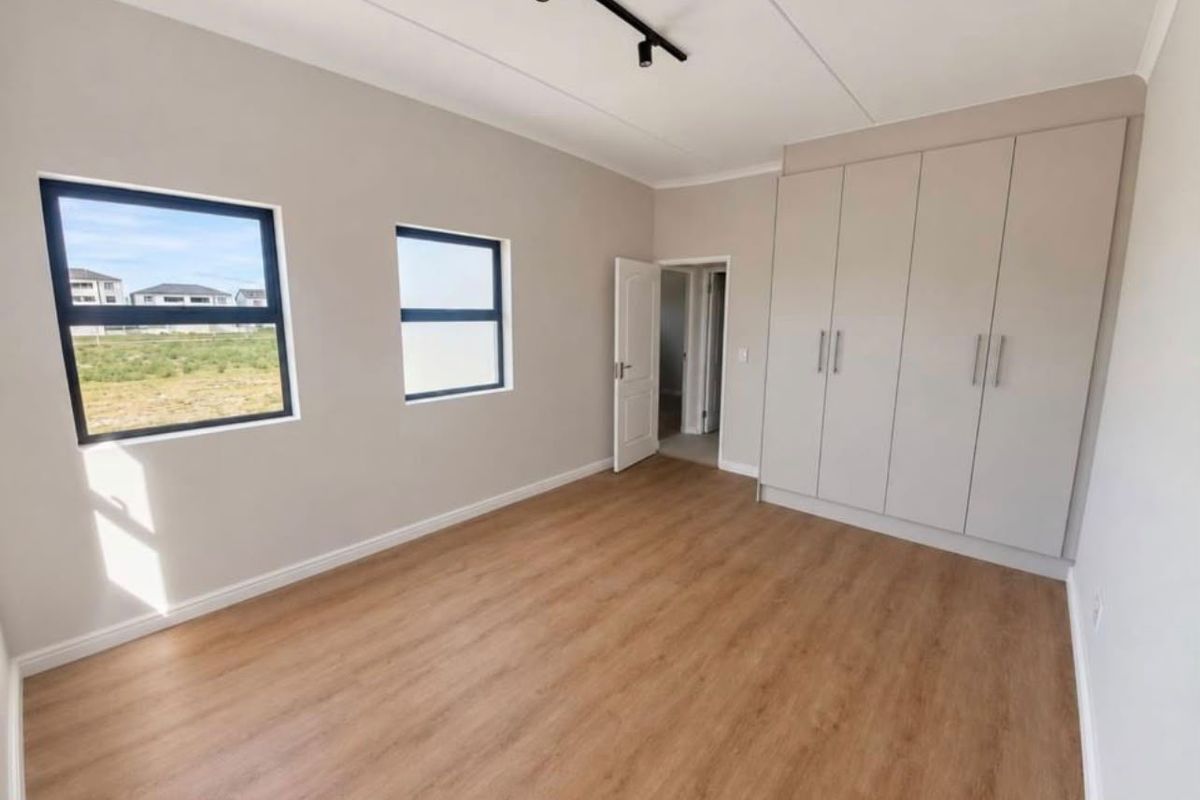 A bright, modern bedroom featuring neutral walls, light wood-look laminate flooring, built-in cupboards, and contemporary track lighting.