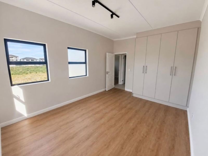 A bright, modern bedroom featuring neutral walls, light wood-look laminate flooring, built-in cupboards, and contemporary track lighting.