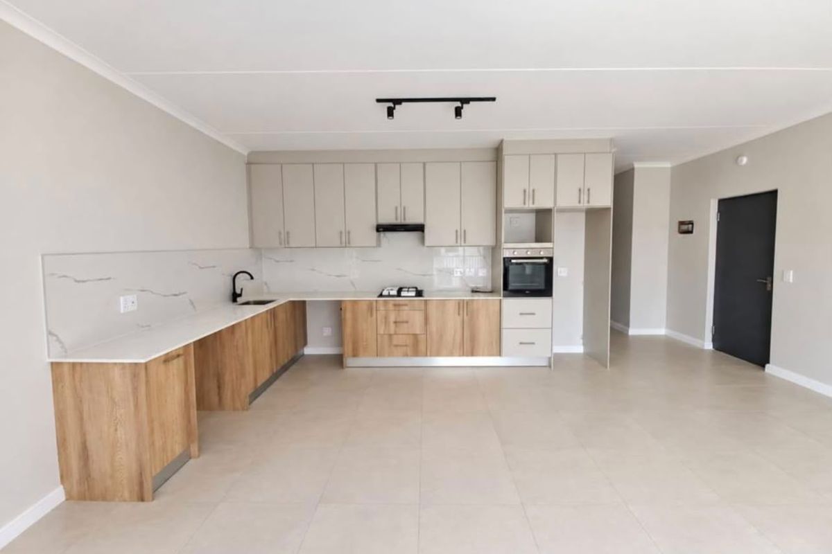 Modern open-plan kitchen featuring two-tone cabinetry, stone countertops, built-in oven, gas hob, and sleek tiled flooring in a bright, spacious living area.