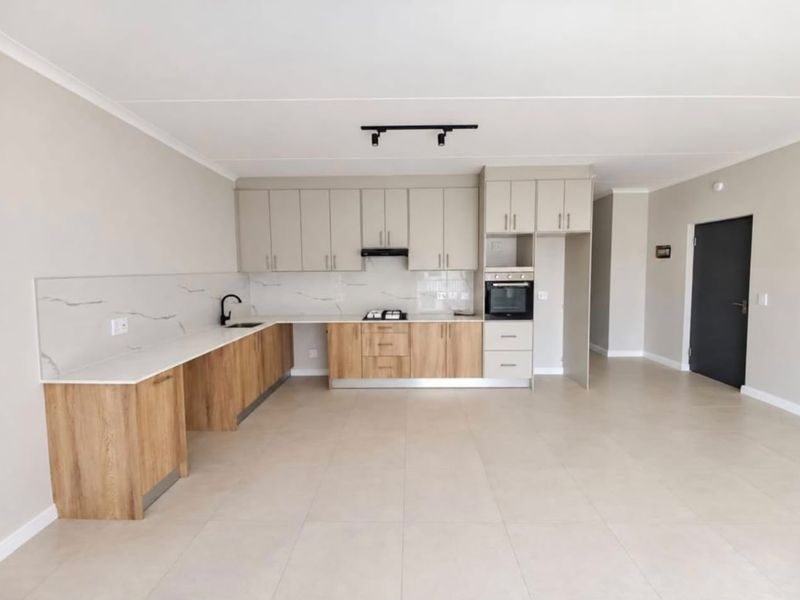 Modern open-plan kitchen featuring two-tone cabinetry, stone countertops, built-in oven, gas hob, and sleek tiled flooring in a bright, spacious living area.