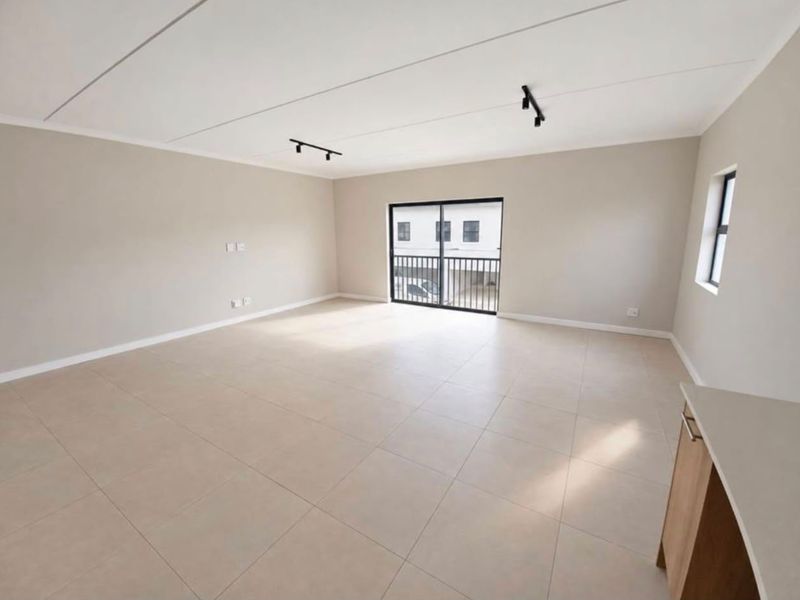 Spacious open-plan living area featuring neutral tiled flooring, modern track lighting, and a sliding glass door leading to a balcony.