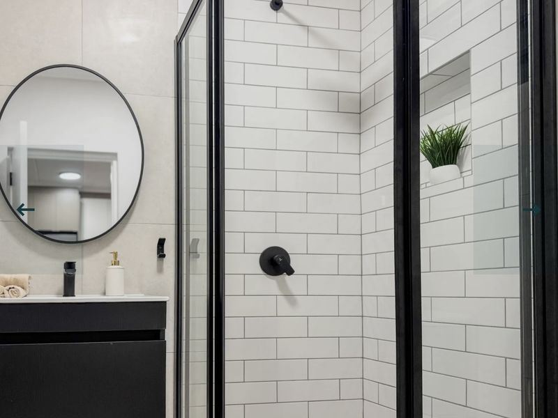 Modern bathroom featuring a sleek vanity, black fixtures, a glass-enclosed shower with subway tiling, and a recessed niche.