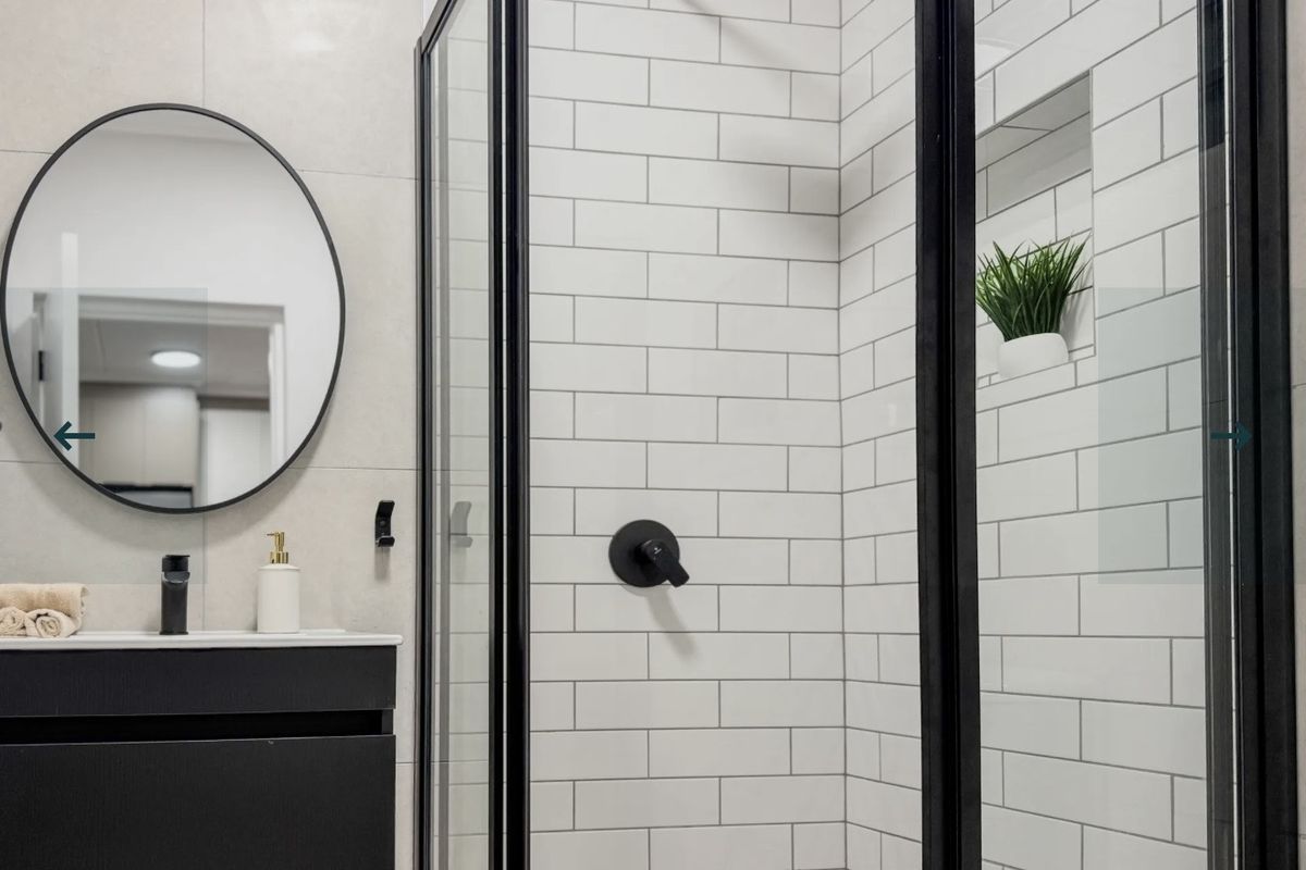Modern bathroom featuring a sleek vanity, black fixtures, a glass-enclosed shower with subway tiling, and a recessed niche.