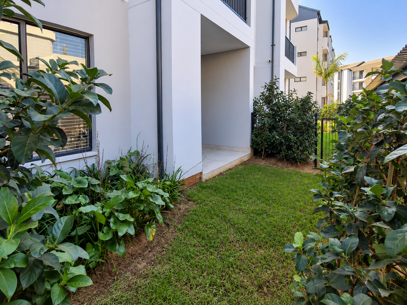 A well-maintained ground floor apartment exterior featuring a private garden area and a tiled patio space.
