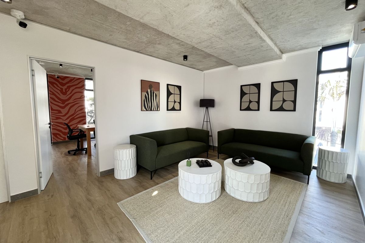 Modern living room featuring an exposed concrete ceiling, laminate flooring, and large windows, creating a bright and contemporary atmosphere.