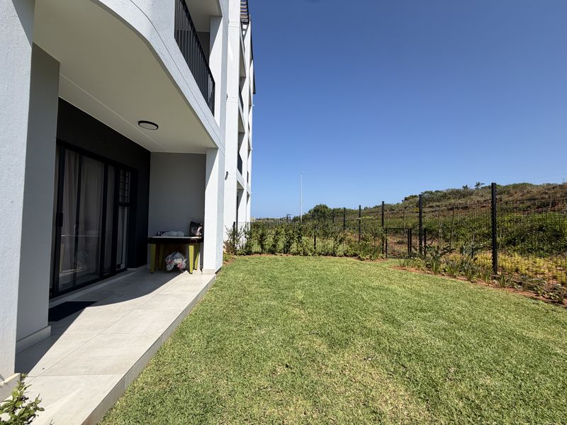 A ground floor apartment featuring a tiled patio area leading onto a private, well-maintained lawn with secure perimeter fencing.