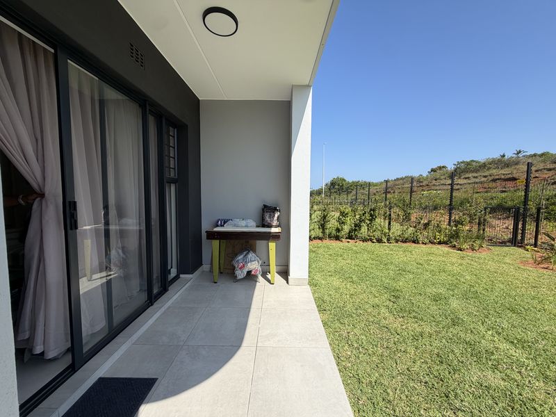 A covered patio featuring modern tiled flooring and large sliding glass doors, overlooking a private garden area with perimeter fencing.
