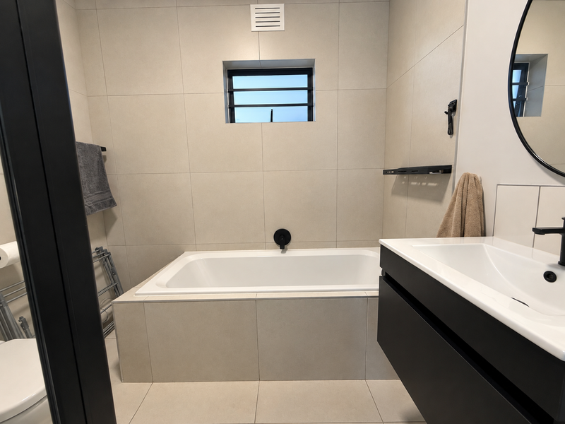 Modern bathroom featuring a built-in bathtub, wall-mounted vanity with basin, and contemporary black matte fixtures, complemented by neutral floor-to-ceiling tiling.