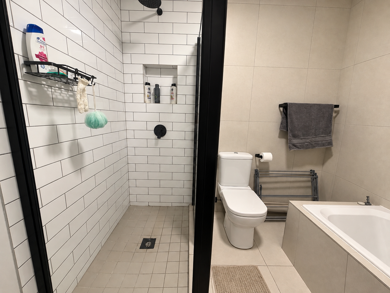 Modern bathroom featuring a walk-in shower with subway tiles, black fixtures, a separate bathtub, and a toilet with large format wall tiles.
