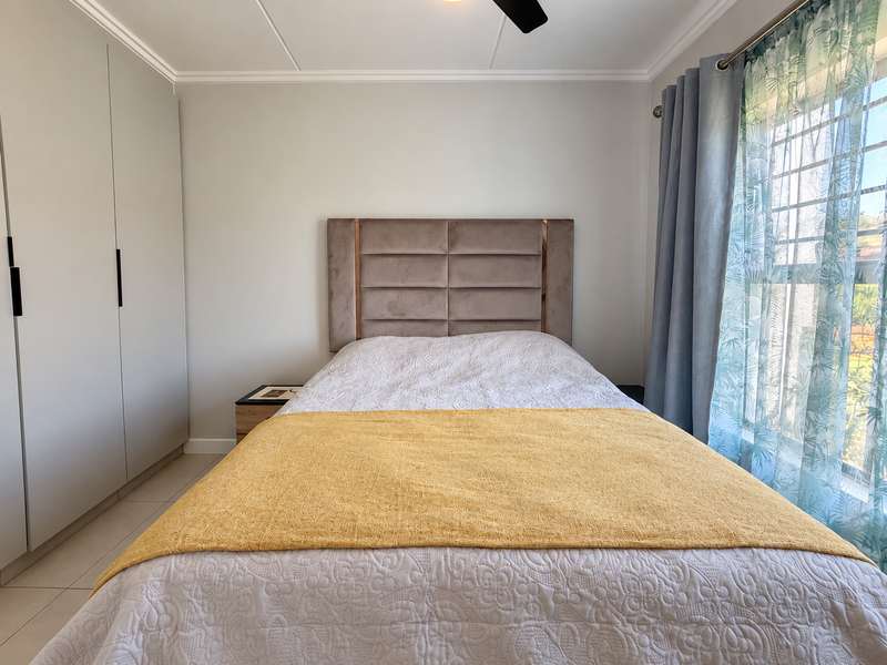 A well-maintained bedroom featuring built-in cupboards, tiled flooring, and a ceiling fan, offering a clean and functional living space.
