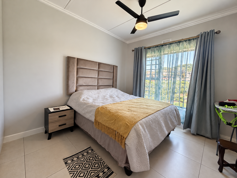A well-maintained bedroom featuring tiled flooring, a ceiling fan, and a large sliding glass door that provides natural light and outdoor views.