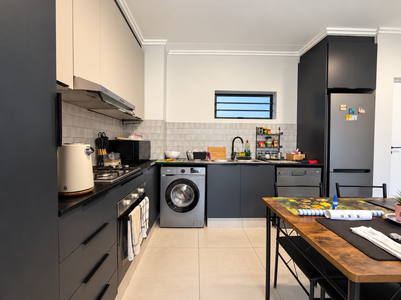 Modern kitchen featuring dark cabinetry, integrated appliances including a washing machine and dishwasher, gas hob, and tiled backsplash.