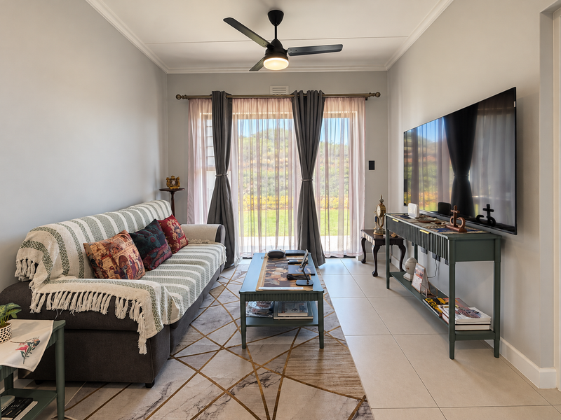 A well-maintained living room featuring tiled flooring, a ceiling fan, and a large sliding glass door providing natural light and garden access.