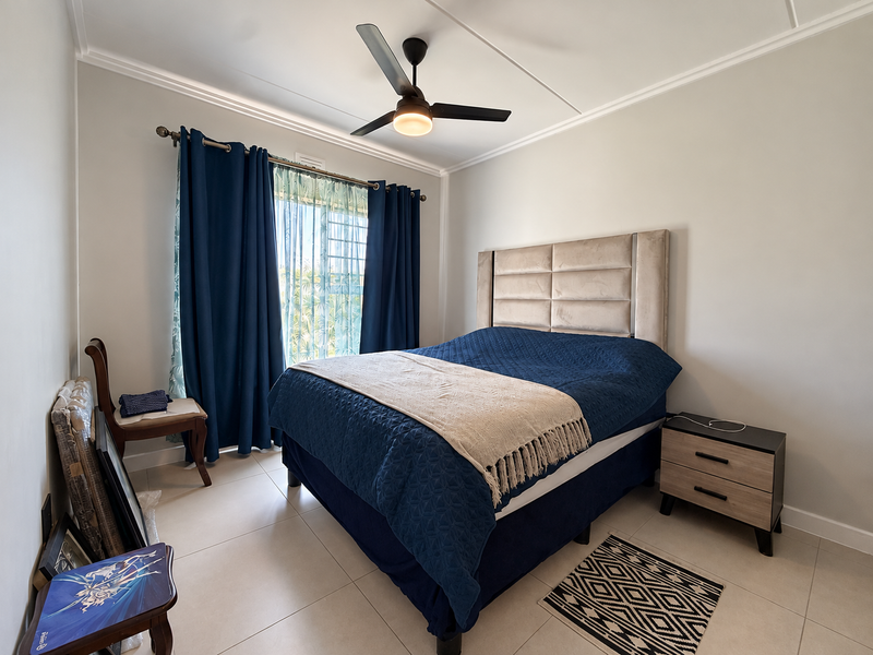 A well-maintained bedroom featuring neutral tiled flooring, crown molding, and a central ceiling fan, offering a clean and functional living space.