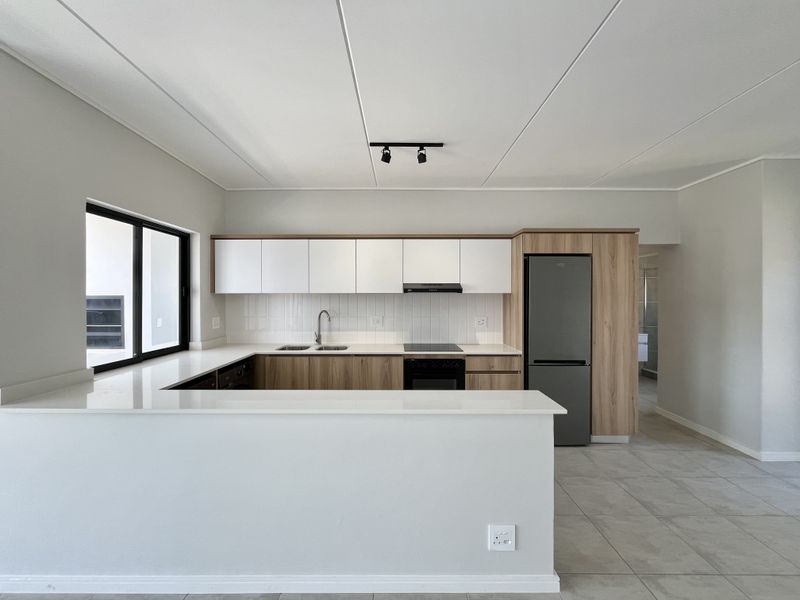 Modern, well-maintained kitchen featuring quartz countertops, integrated cabinetry, built-in oven, electric hob, and sleek tiled finishes in a clean, open-plan layout.
