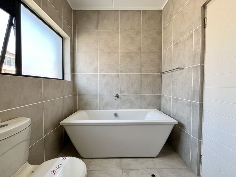 Modern bathroom featuring a clean freestanding bathtub, neutral wall tiling, and a frosted window for privacy and natural light.