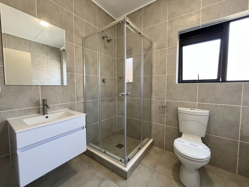 A modern, well-maintained bathroom featuring a glass shower enclosure, wall-mounted vanity with basin, and neutral floor-to-ceiling tiling.