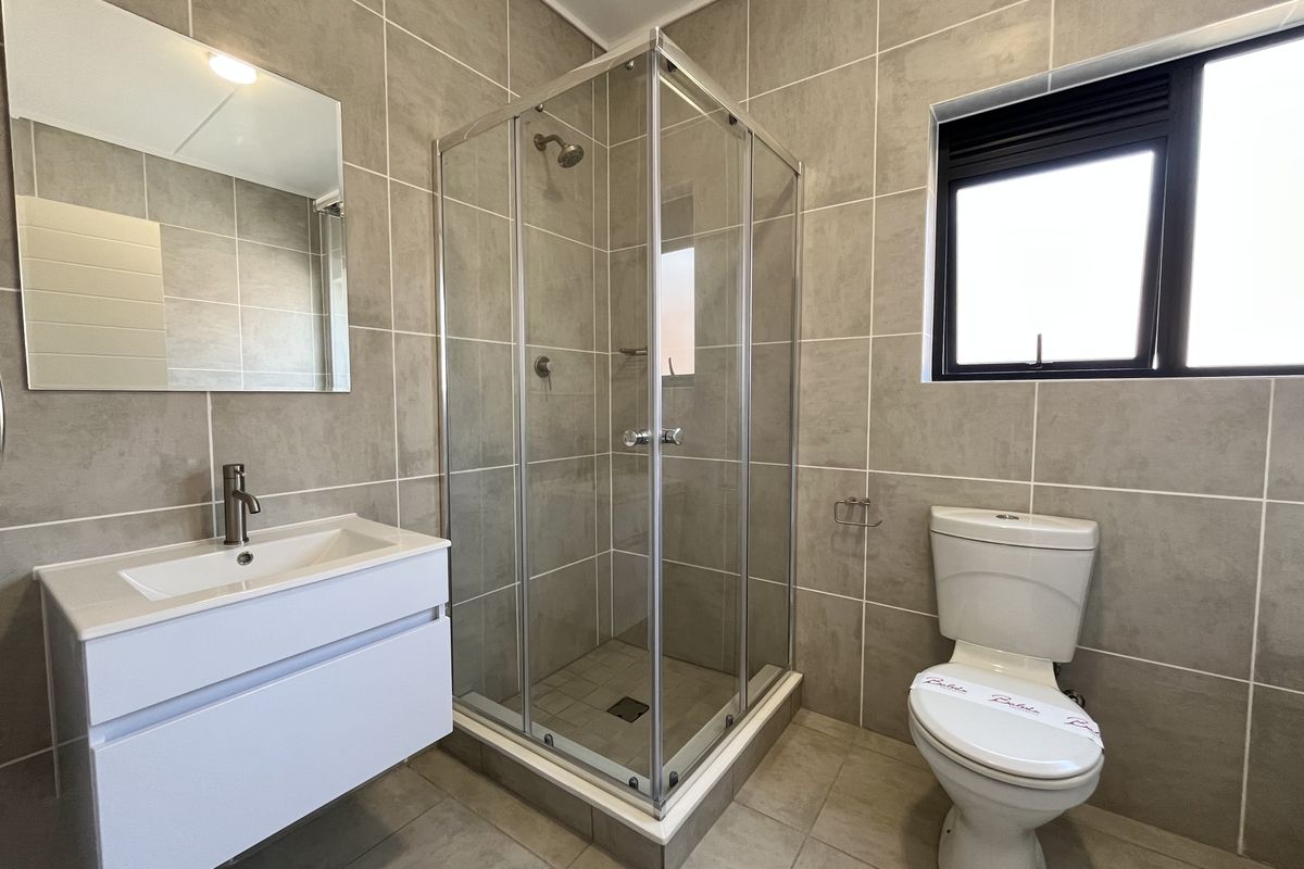 A modern, well-maintained bathroom featuring a glass shower enclosure, wall-mounted vanity with basin, and neutral floor-to-ceiling tiling.