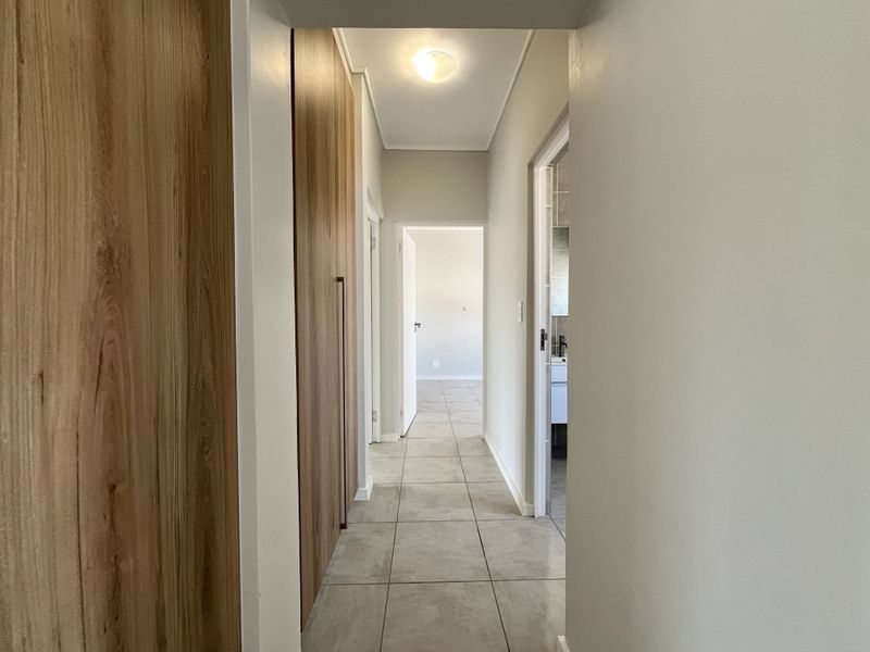 A clean, well-lit hallway featuring modern tiled flooring and integrated floor-to-ceiling wooden cabinetry, providing ample storage space.