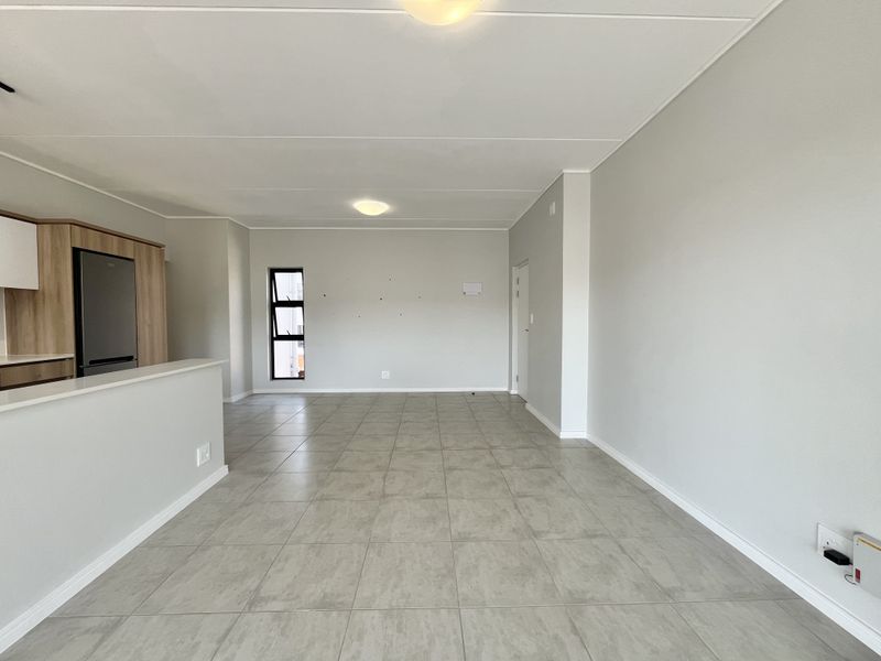 Spacious open-plan living area featuring neutral tiled flooring, clean walls, and a modern kitchen corner, offering a versatile blank canvas for interior design.