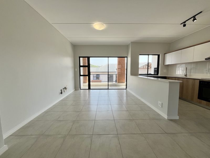 A bright and modern open-plan living and kitchen area featuring neutral tiled flooring, contemporary cabinetry, and direct access to a private balcony.