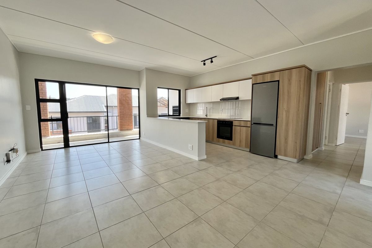Modern open-plan living area featuring a sleek kitchen with built-in appliances, tiled flooring, and large sliding doors leading to a balcony.