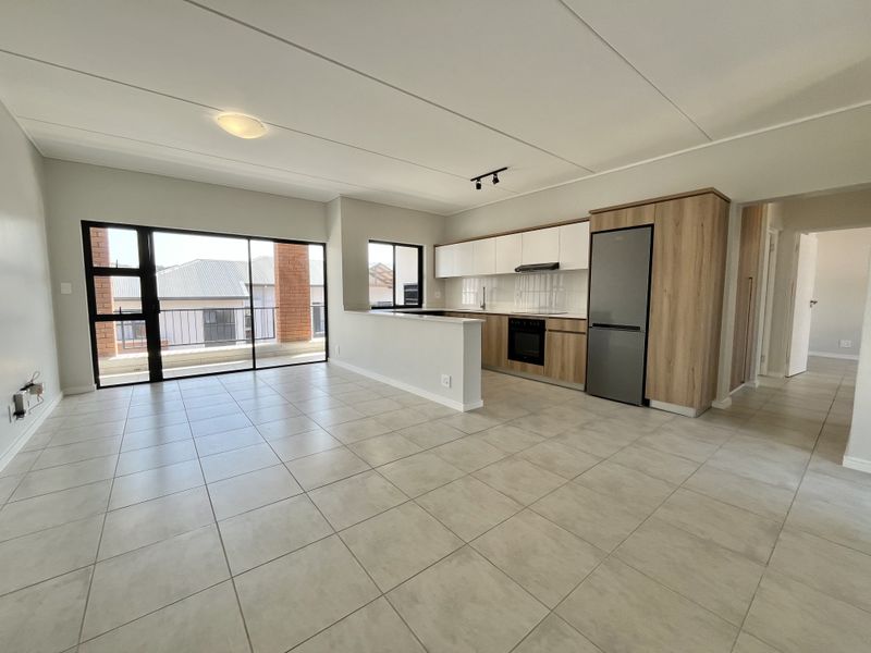 Modern open-plan living area featuring a sleek kitchen with built-in appliances, tiled flooring, and large sliding doors leading to a balcony.