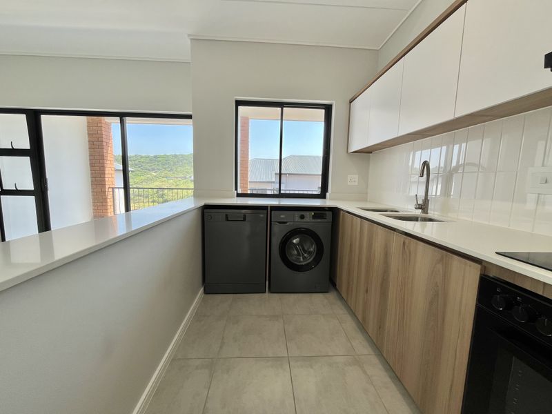 Modern kitchen featuring sleek wood-finish cabinetry, stone countertops, tiled backsplash, and integrated appliances, with natural light and views through large windows.