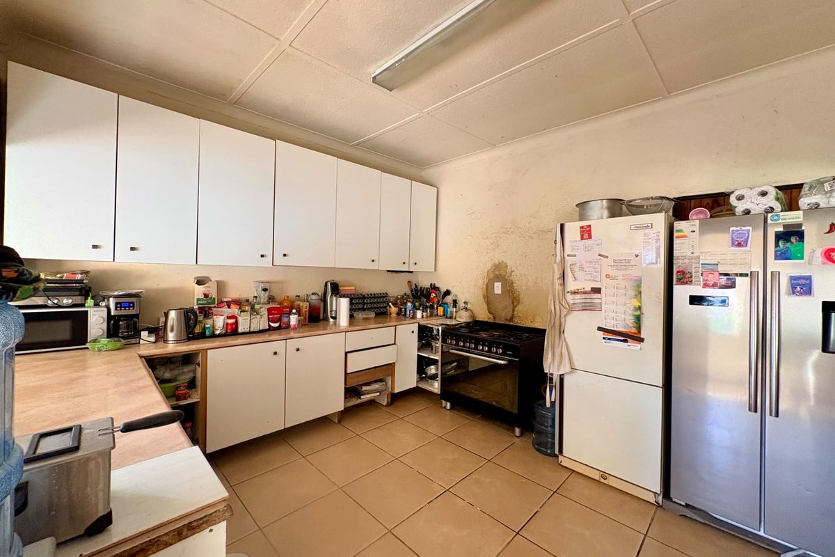 A functional kitchen featuring white cabinetry, laminate countertops, gas stove, and tiled flooring, currently requiring cosmetic updates and wall repairs.