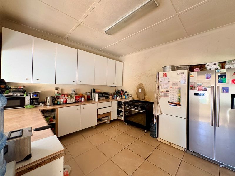 A functional kitchen featuring white cabinetry, laminate countertops, gas stove, and tiled flooring, currently requiring cosmetic updates and wall repairs.