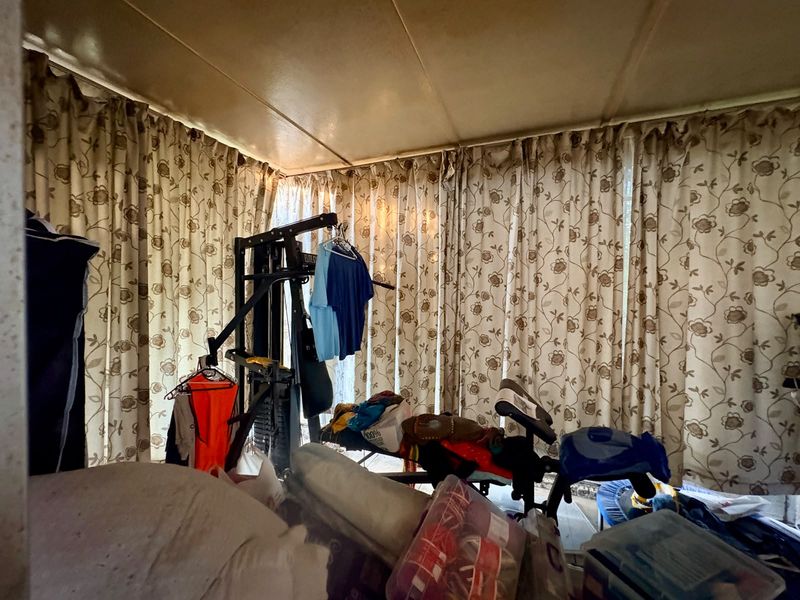 A bedroom space featuring full-length window curtains, currently utilized for storage and exercise equipment.