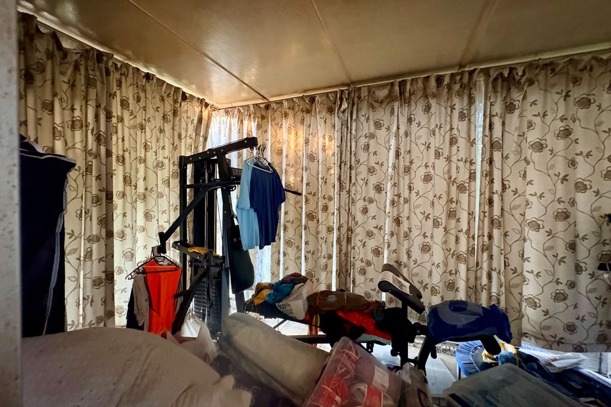 A bedroom space featuring full-length window curtains, currently utilized for storage and exercise equipment.