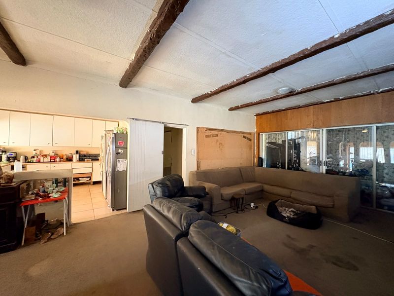 Open plan living and kitchen area featuring exposed timber ceiling beams, tiled kitchen floors, and direct access to the outdoors via sliding glass doors.