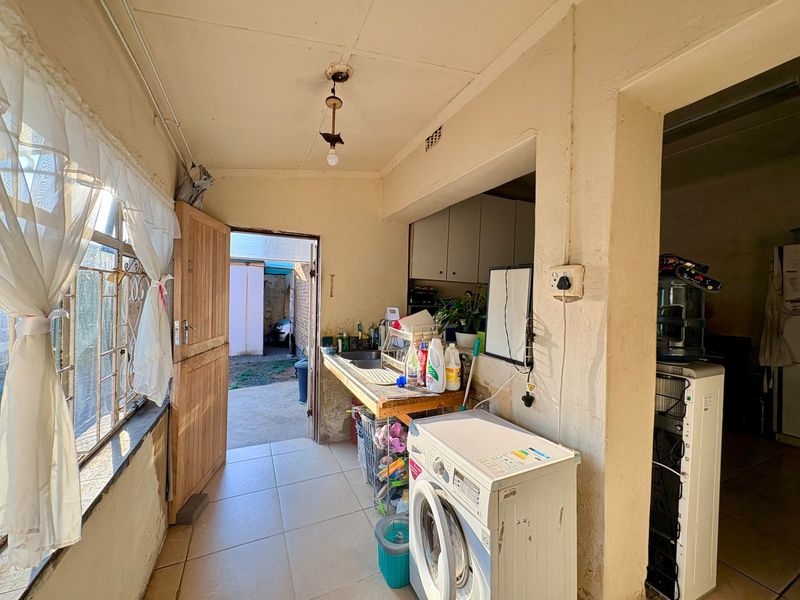 A functional laundry area featuring tiled floors, a built-in sink, and direct access to the rear exterior, requiring cosmetic updates and maintenance.